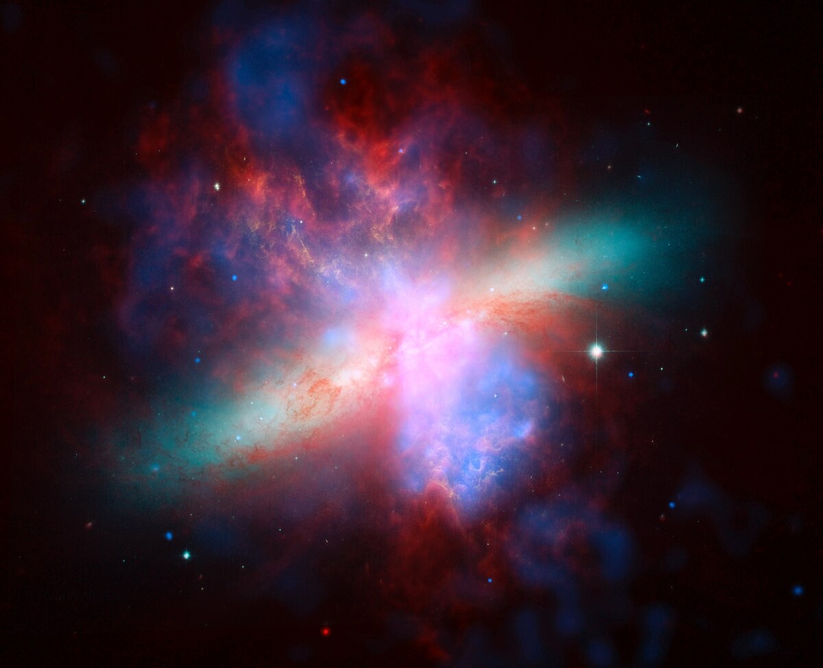 このほど巨大フレアが発生したマグネターがあると考えられるM82銀河。NASAの宇宙望遠鏡スピッツァー、ハッブル、チャンドラがそれぞれ異なる波長で撮影した画像を合成した擬似カラー画像。（PHOTOGRAPH BY NASA/JPL-CALTECH/STSCI/CXC/UOFA/ESA/AURA/JHU）